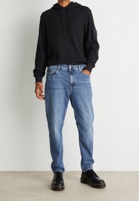 Svart huva tröja, blåa denimjeans och svarta snörskor. Enkel design, avslappnad passform, ribbad struktur och synliga sömmar.