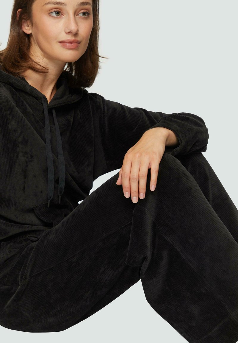 Czarny zestaw odzieży domowej składający się z hoody z regulowanym kapturem oraz spodni o szerokich nogawkach, wykonany z miękkiego, teksturowanego materiału. Minimalistyczny design z luźnym krojem.