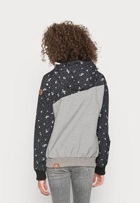 Sweatshirt com capuz, apresentando um tecido preto com padrão de estrelas nos ombros e mangas, com um corpo cinza e punhos e barra canelados.