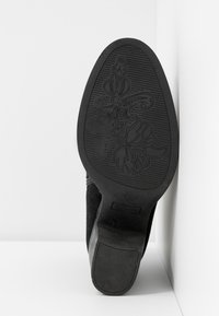 Suela de zapato negra con un diseño texturizado que presenta patrones florales y surcos paralelos, hecha de goma con un acabado mate.