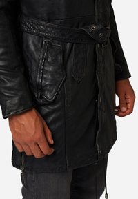 Schwarze Lederjacke mit einem strukturierten Gürtel, seitlichen Taschen und sichtbaren Nähten. Sie hat einen Reißverschluss am Saum und eine glatte Oberfläche.