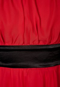 Tissu rouge avec texture froncée présentant une large ceinture noire lisse qui serre le matériau.