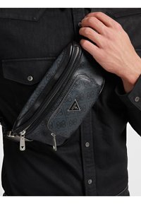 Borsa crossbody a motivo nero e blu con rifiniture in pelle, hardware argentato e diverse tasche con zip, indossata sopra una maglietta nera.