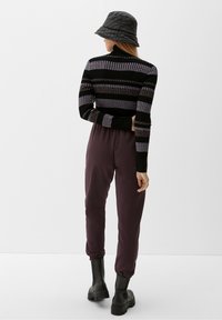Maglione a righe nero e viola a maglia con collo alto, abbinato a pantaloni tuta elasticizzati viola scuro e stivaletti neri.