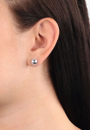 Pendiente de plata con forma esférica pulida. Textura suave, diseño minimalista y superficie reflectante, llevado en el lóbulo.