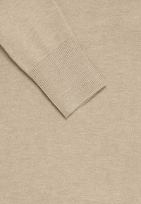Manica di un maglione a maglia beige con polsino a coste su uno sfondo di tessuto a maglia beige coordinato.