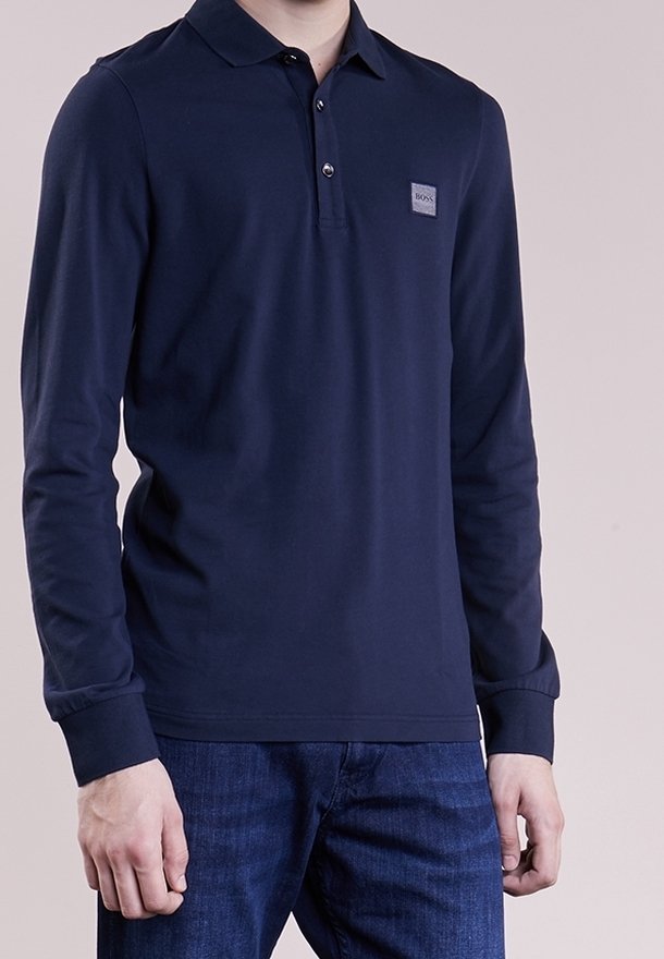 Polo-shirt à manches longues bleu marine avec col et patte de boutonnage à trois boutons, affichant un petit patch de marque sur la poitrine gauche. Tissu en mélange de coton.