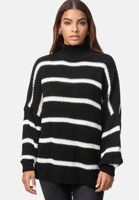 Maglione lavorato a maglia a righe bianche e nere con colletto alto, vestibilità ampia e polsini a coste. Presenta una trama spessa e maniche larghe.