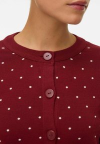 Cárdigan burdeos con lunares blancos, escote redondo y dos botones grandes. Tejido de punto suave y silueta ajustada.
