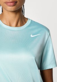 Világoskék Nike póló, amely kerek nyakkivágással, rövid ujjakra, sima textúrára és egy kis fehér logóra van a bal mellen.