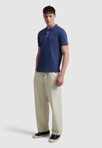 Polo-shirt bleu marine avec trois boutons, manches courtes et un petit logo brodé. Associé à un pantalon beige clair à cordon de serrage et des baskets bleu marine.