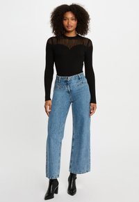 Top lungo a maniche nere a coste con dettagli a strisce trasparenti, abbinato a jeans in denim a vita alta, larghi e di un lavaggio chiaro, e stivali neri con tacco.