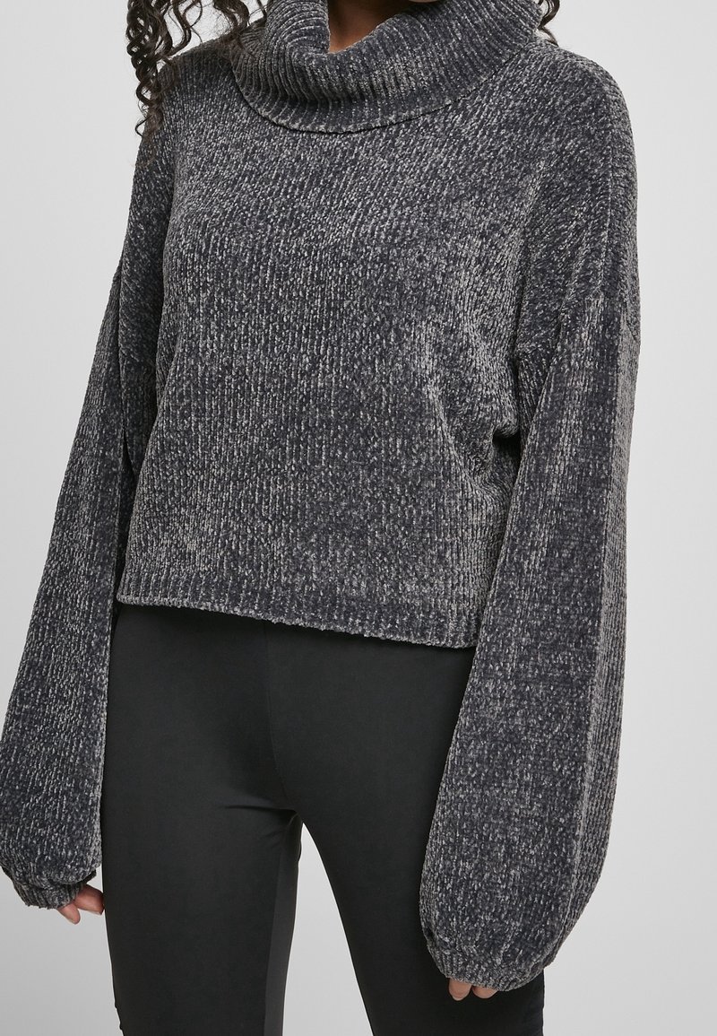 Personne portant un pull gris foncé côtelé à col roulé avec de longues manches bouffantes et un pantalon noir ajusté.