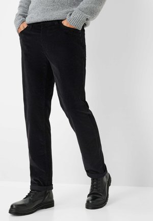 Pantaloni di velluto a coste neri con vestibilità slim, dotati di tasche laterali e orli arrotolati, abbinati a stivali in pelle neri con lacci.
