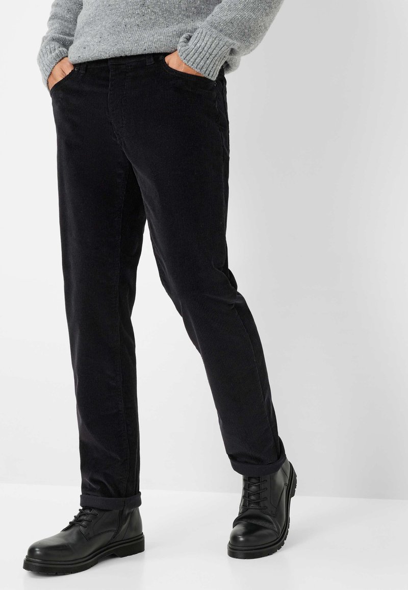 Zwarte corduroy broek met een slim fit, voorzien van zijzakken en opgerolde boorden, gecombineerd met zwarte leren veterschoenen.