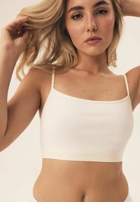 Lekki, biały crop top z cienkimi ramiączkami, charakteryzujący się miękką, gładką fakturą i dopasowanym krojem. Zawiera kontrastowy, jasny pasek na dole.