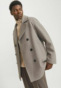 Manteau en laine gris avec un design croisé, boutons noirs et col cranté, porté sur un pull beige texturé.