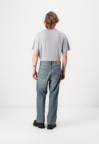 Lett grå T-skjorte i avslappet passform, kombinert med baggy jeans i middels vask. Merkbare sømmer på baklommene og lærmerkelapp. Sorte kraftige sko.