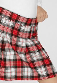 Czerwona kraciasta spódnica plisowana z elastycznym pasem, w białe, czarne i czerwone kratki. Tkanina ma fakturę, prezentując klasyczny wzór tartan.