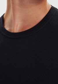 Sort ribbet bomulds t-shirt med rund halsudskæring. Nærbillede der viser tekstur og fine sømme omkring kraven.