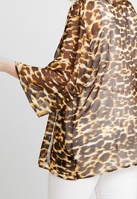 Bruine en beige doorschijnende kimono met een luipaardprint, voorzien van wijde mouwen en een losse pasvorm, met de nadruk op lichtgewicht stof en een vloeiende uitstraling.