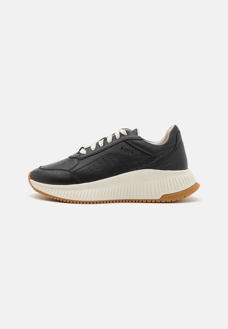 Baskets en cuir noir avec lacets blancs, panneau latéral perforé, semelle épaisse couleur crème, et semelle extérieure en gomme, marquées "BOSS" sur le côté et la semelle.