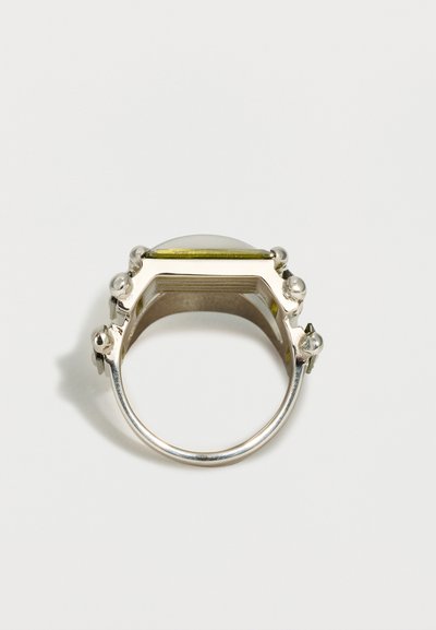 Srebrn prstan s širokim pravokotnim vrhom, okrašen z izbočenimi sferičnimi detajli ob robovih, na enostavni belem ozadju.