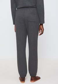 Graue gerippte Lounge-Hosen mit einer lockeren Passform, ausgestattet mit einem elastischen Bund und einer einzelnen Gesäßtasche. Die Bündchen verjüngen sich an den Knöcheln.