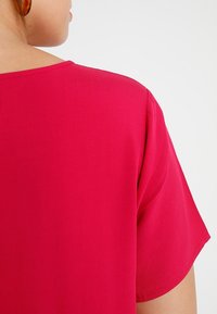 Maglietta a maniche corte, con scollo rotondo, in tessuto rosa brillante. Tessuto liscio con una vestibilità comoda, caratterizzata da un design pulito senza decorazioni.