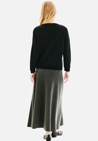 Pull en maille noir à manches longues, associé à une jupe en laine grise fluide atteignant le mollet, portée avec des chaussures noires simples.