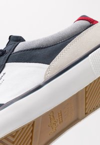 Tenisky z plátna a semiše se směsí námořnické modré, bílé a béžové barvy, s vzorovanou šedou látkou na vršku a gumovou podrážkou.