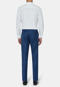 Witte blouse met lange mouwen en een verspreide kraag, gedragen met aansluitende blauwe broek. De blouse heeft een gladde textuur, terwijl de broek een subtiel patroon heeft.