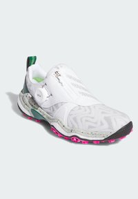 Vit träningsskor med en texturerad design, BOA-snörningssystem och en sula med rosa fläckar. Har en slip-on stil och gröna detaljer.