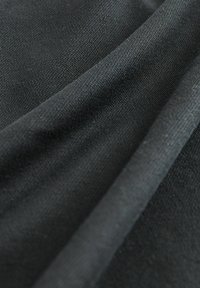 Czarna tkanina o teksturowanej powierzchni, z gładkimi fałdami i lekko odbijającym światło połyskiem, idealna do różnych zastosowań tekstylnych.
