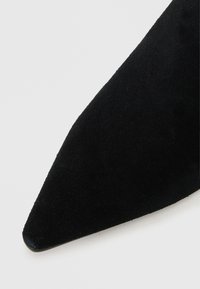 Black suede pointed-toe shoe with a smooth texture and tapered shape. Features a low-profile design and subtle stitching along the edge.