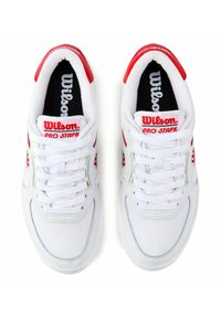 Baskets de sport blanches avec accents rouges et semelles intérieures noires, dotées d'un dessus en maille et cuir, d'un système de laçage et de la marque "Wilson Pro Staff".