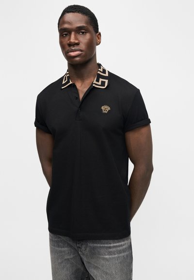 Juoda polo marškinėliai su raštuotu smėlio spalvos apykakle, kairėje krūtinės pusėje su liūto emblemą. Trumpomis rankovėmis, klasikinio stiliaus ir iš medvilnės.