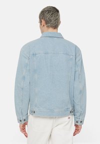 Ljusblå denimjacka med klassisk krage, knappade ärmslut och synlig sömnad. Slät textur med avslappnad passform.