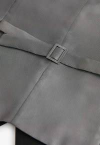 Grauer Stoff mit strukturiertem Muster, ausgestattet mit einem flachen Riemen, der mit einer grauen Metallschnalle gesichert ist, sowie gefalteten und geschichteten Designelementen.