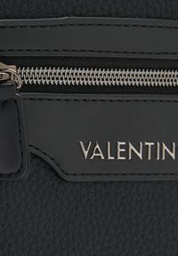 Borsa in pelle nera con superficie texture, zip argentata e un logo "VALENTINO" in evidenza. Design liscio e elegante con accenti minimi.