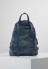 Mochila de mezclilla azul con acabado texturizado, con correas ajustables, una parte superior redondeada y un pequeño bolsillo lateral con cremallera.