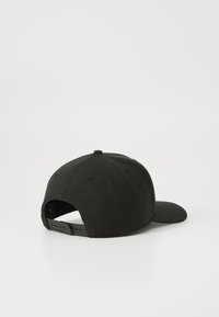 Gorra snapback negra hecha de algodón. Presenta una visera plana, una correa de plástico ajustable en la parte posterior y orificios de ventilación cosidos.