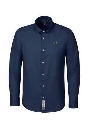 Marineblaues langärmliges Hemd mit Knöpfen und Kragen, weißen Knöpfen, gesticktem Logo auf der Brust und einem Pflegeetikett nahe dem unteren Saum.