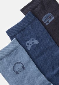 Três pares de meias em diferentes tons de azul com padrões: um auricular, um controlador de jogo e um hambúrguer, todos em um tricot macio e texturizado.