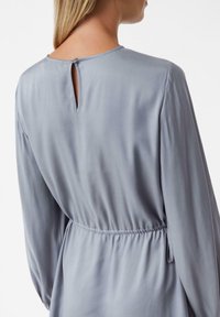 Sukienka z długim rękawem w jasnoszarym satynie, z otworem w kształcie łezki z tyłu oraz elastycznym pasem dla podkreślenia talii.