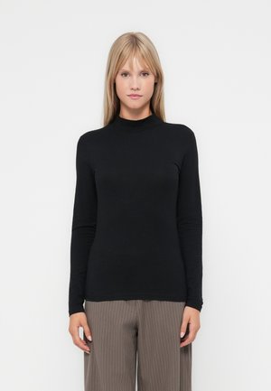 Svart langermet topp med høy hals, laget av myk stoff; tettsittende design. Brukt med stripede, vide bukser; minimalistisk stil.