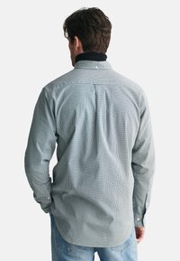 Langärmliges Hemd mit Knöpfen im grün-weiß karierten Muster. Verfügt über einen Kragen mit marineblauen Akzenten, eine Falte im Rücken und knöpfbare Manschetten.