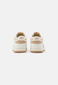 Scarpe da ginnastica Nike con tomaia in pelle bianca, dettagli beige e suola in gomma marrone chiaro testurizzata. Presentano il marchio "Nike" sul tallone.