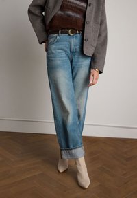 Lichtblauwe, vervaagde wijde jeans met omgeslagen boorden en een bruine leren riem. Gecombineerd met beige hoge hakken en een grijze buitenjas.