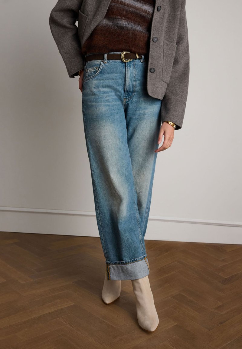 Lichtblauwe, vervaagde wijde jeans met omgeslagen boorden en een bruine leren riem. Gecombineerd met beige hoge hakken en een grijze buitenjas.